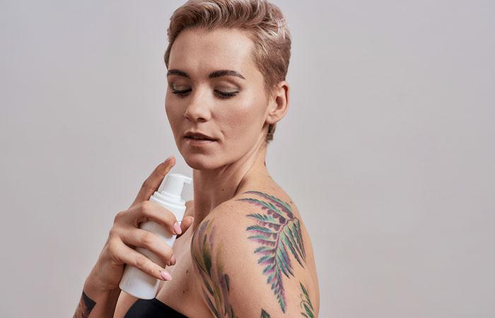 Hand applying a fragrance-free moisturizer on a healed watercolor tattoo to maintain color.