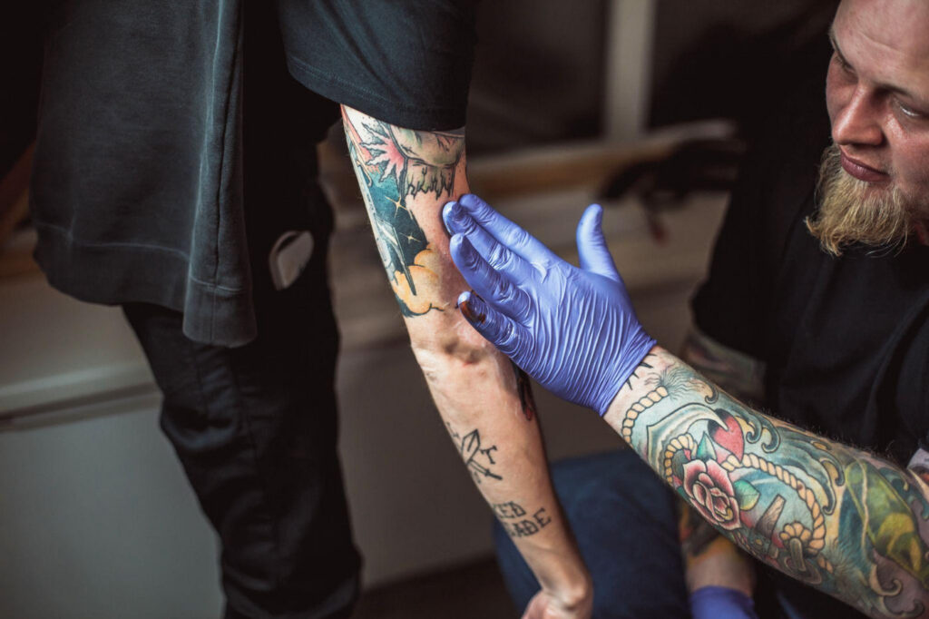 A tattoo artist checking a client's healing tattoo for any issues