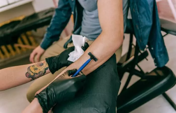 Cạo lông tay bằng dao cạo dùng một lần trước khi xăm.