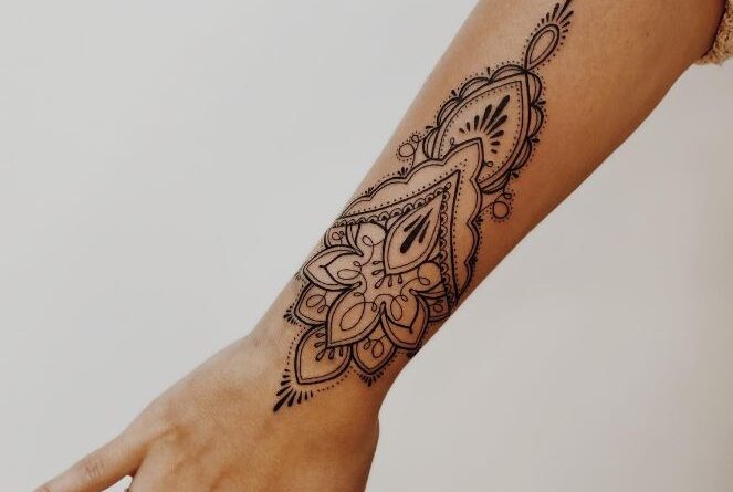 Tattoo artist sketching an ornamental mandala design on paper with fine liner pens.