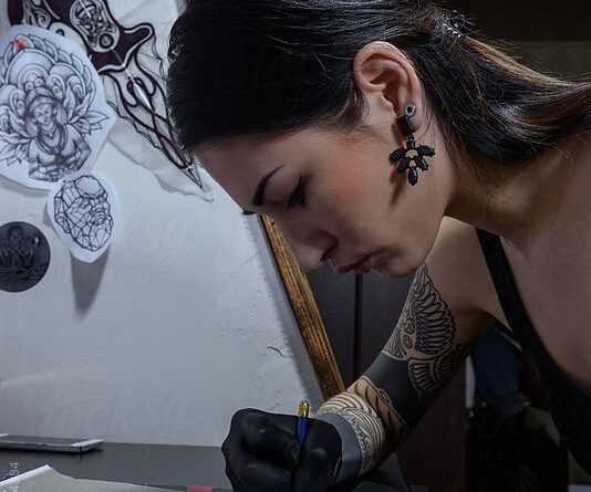 A tattoo artist sketching a tribal design on paper with fine liner pens.