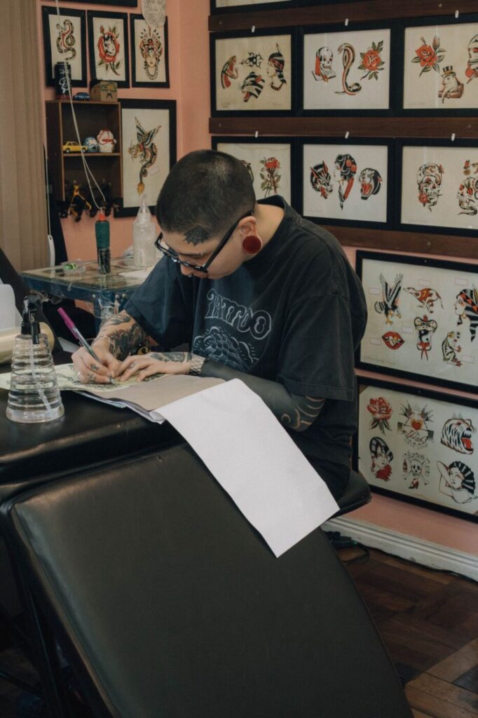 A bustling walk-in tattoo studio in Hanoi with a waiting area and flash sheets on the wall.