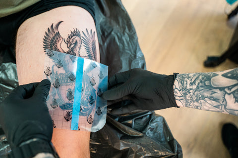 A tattoo stencil being placed on a client's arm with a ruler for precise positioning.