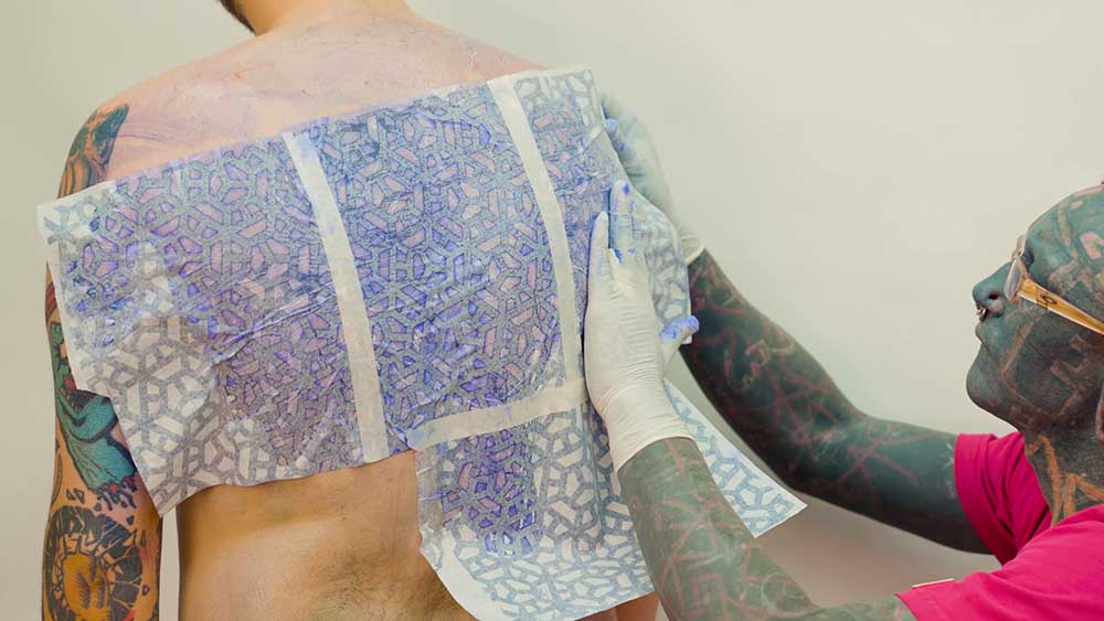 Tattoo artist carefully placing a stencil on the client's ribcage to follow the body's curve.